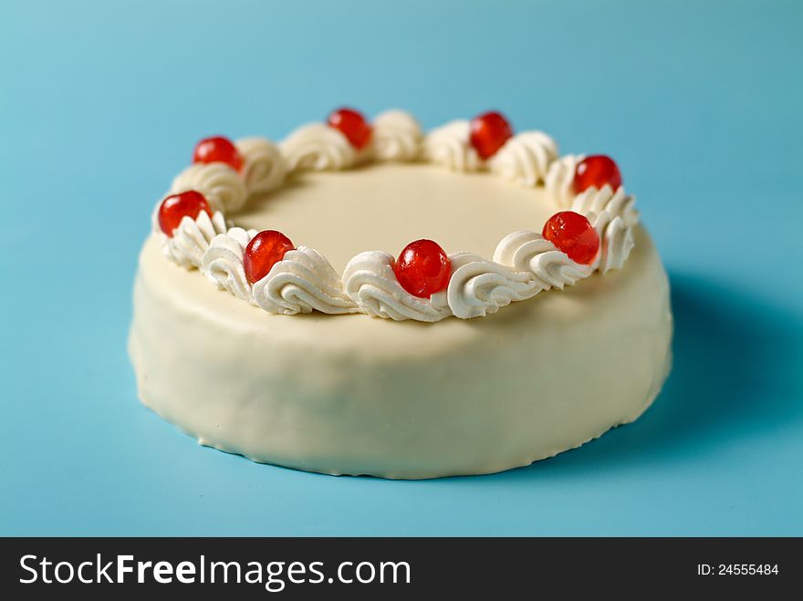 White cake with cherries on light blue table. White cake with cherries on light blue table