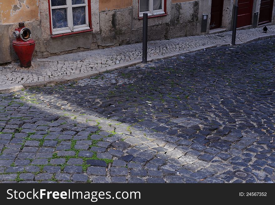 Cobblestone street with a ray of sunshine, with an old red fire hydrant, in Lisbon. Cobblestone street with a ray of sunshine, with an old red fire hydrant, in Lisbon.