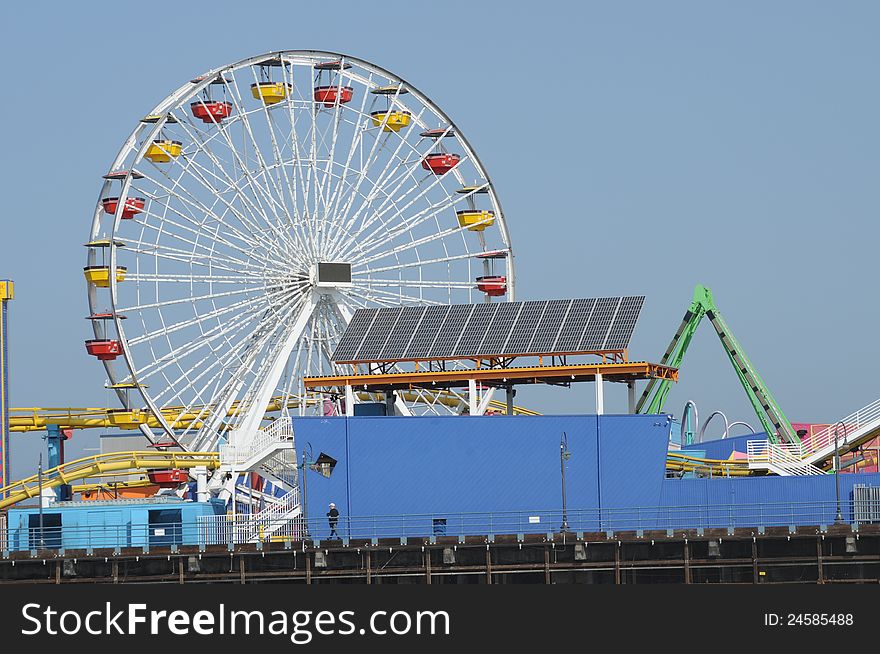 A colorful ferris wheel with red and yellow passenger buckets and solar panels  next to it. A colorful ferris wheel with red and yellow passenger buckets and solar panels  next to it