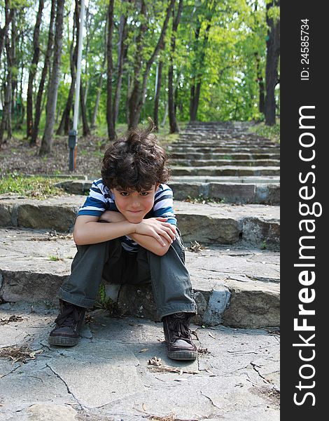 Beautiful smiling boy sitting resting on stone staircase with arms propped on his head. Beautiful smiling boy sitting resting on stone staircase with arms propped on his head