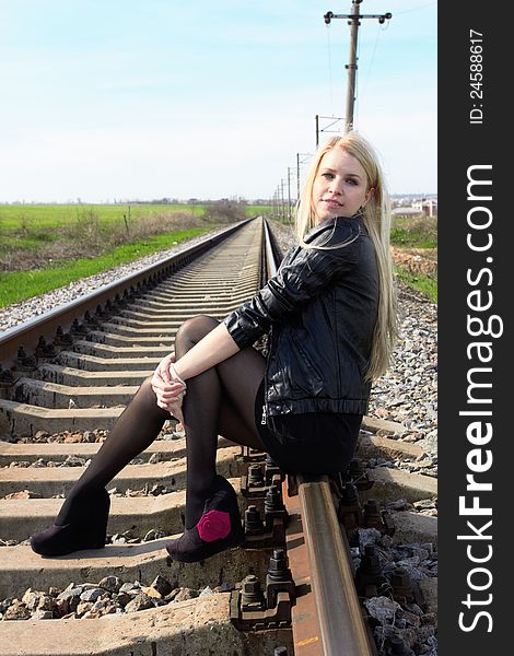 Attractive young girl sitting on railroad tracks