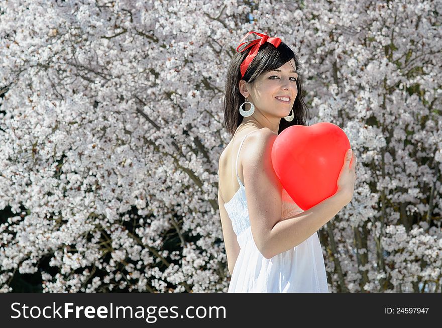 Young beautiful woman with red heart shape balloon and trees in bloom. Young beautiful woman with red heart shape balloon and trees in bloom