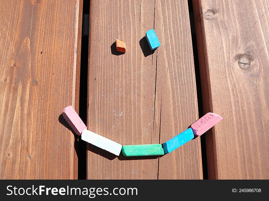 a face made of crayons on a wooden background. happy summer