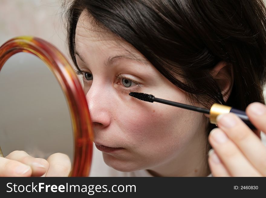 The woman with mascara looks in a mirror