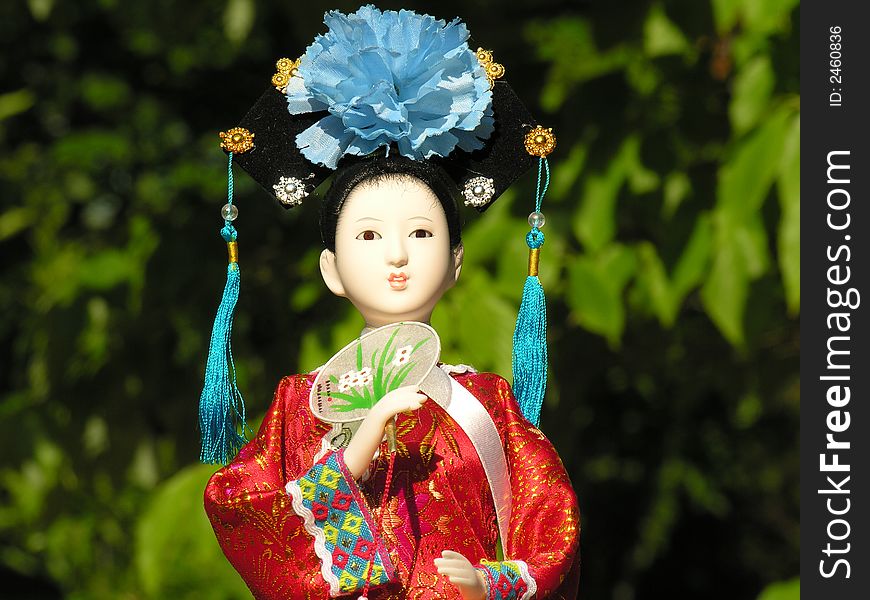 A Geisha doll with green foliage in the background.