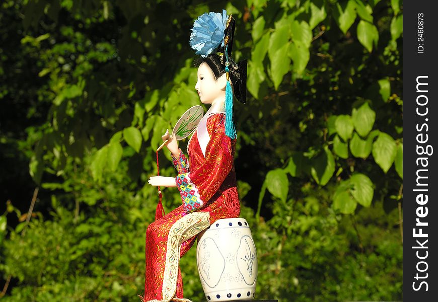 A Geisha doll with green foliage in the background. A Geisha doll with green foliage in the background.