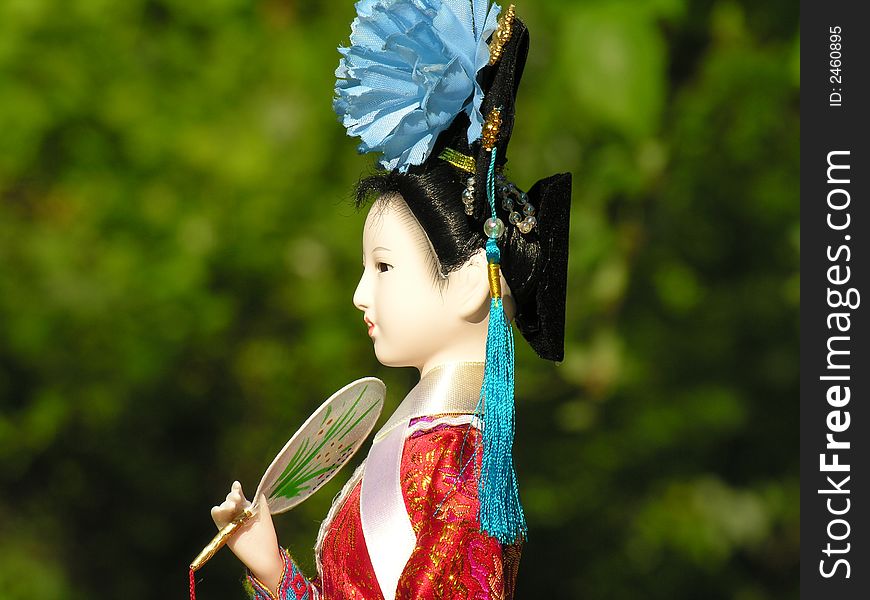 A Geisha doll with green foliage in the background. A Geisha doll with green foliage in the background.