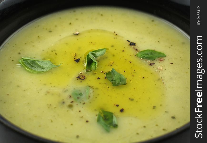 Close-up of cream of zucchini soup in a black bowl with olive oil, pepper and basil on top. Close-up of cream of zucchini soup in a black bowl with olive oil, pepper and basil on top.