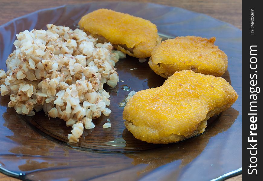 A plate of buckwheat porridge with chicken nuggets standing on a wooden table for the dinner.