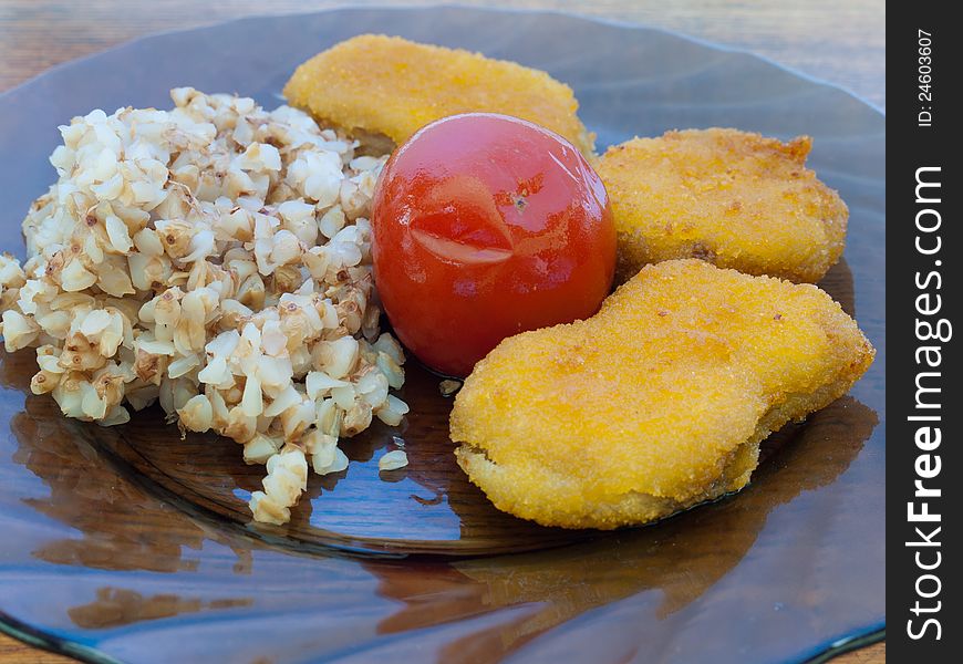 A plate of buckwheat porridge with chicken nuggets and tomato standing on a wooden table for the dinner.