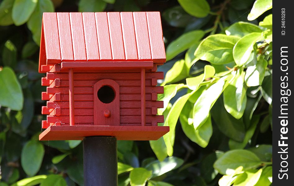 Barn Red Birdhouse Mounted On Pole With Green Leaf Background. Barn Red Birdhouse Mounted On Pole With Green Leaf Background