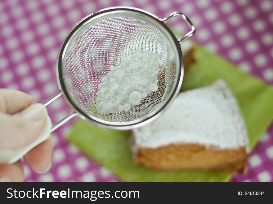 Sieve with powdered sugar and slice of cake