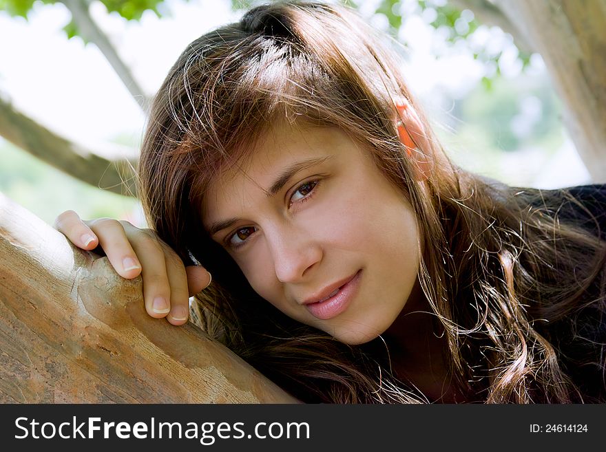 A portrait of a young woman, leaning on a tree and smiling sweetly at the viewer. A portrait of a young woman, leaning on a tree and smiling sweetly at the viewer