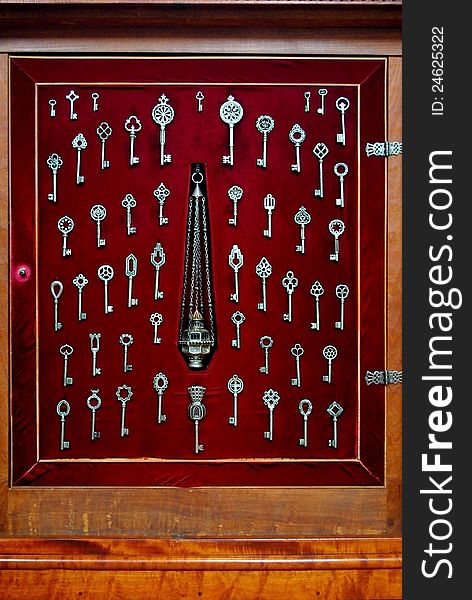 Various sized silver skeleton keys displayed against red velvet in a wood furniture showcase. Various sized silver skeleton keys displayed against red velvet in a wood furniture showcase