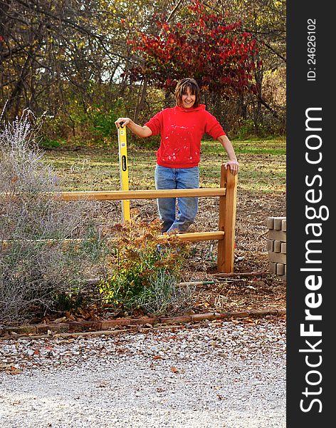 A woman landscaper, level in hand, completes the installation of a split rail fence project. A woman landscaper, level in hand, completes the installation of a split rail fence project