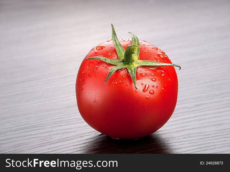 One fresh tomato with drops of water on the wooden background. One fresh tomato with drops of water on the wooden background