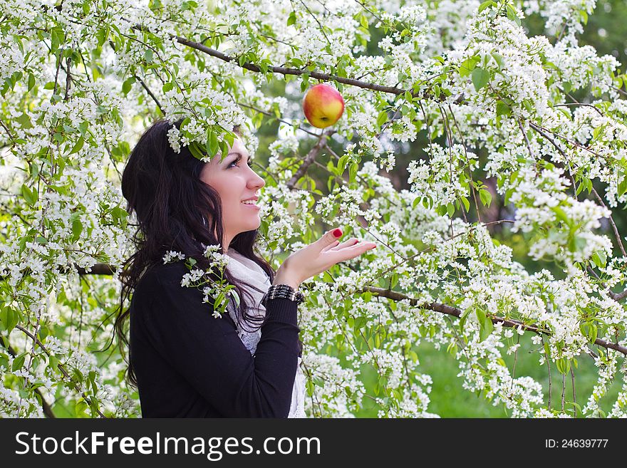 Young woman catching an apple against the backdrop of flowering trees