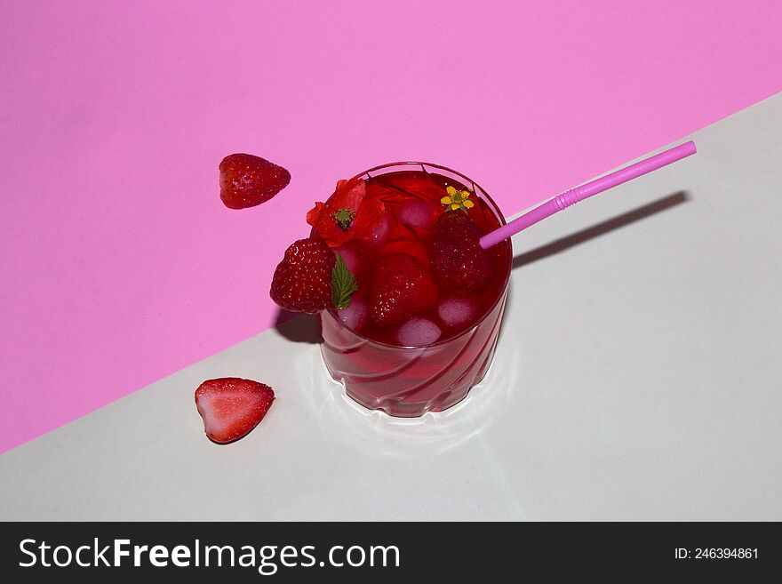 a glass of strawberry juice arranged with flowers and strawberries, next to a glass of strawberries cut in half on a pastel pink-g
