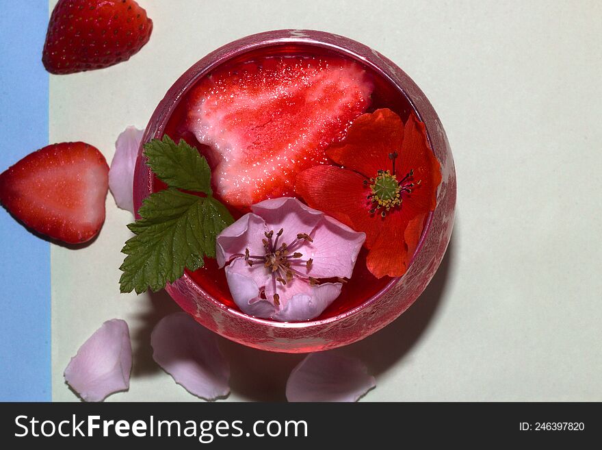 drinking glass of strawberry juice with strawberry and two flower head as decoration, one flower red the other white around the ca