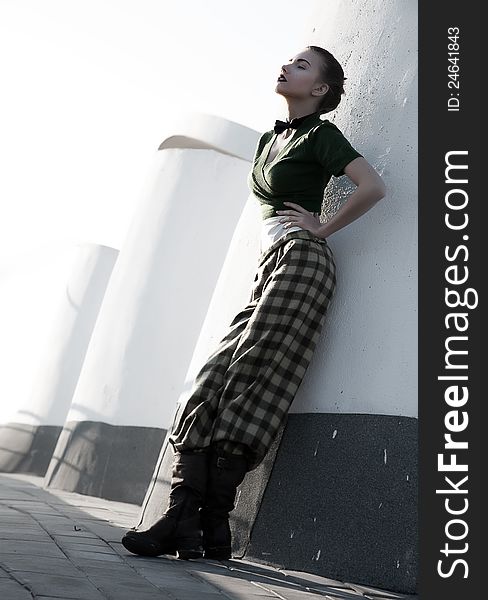 Beautiful young woman in checkered trousers stand leaning on city walls. Beautiful young woman in checkered trousers stand leaning on city walls