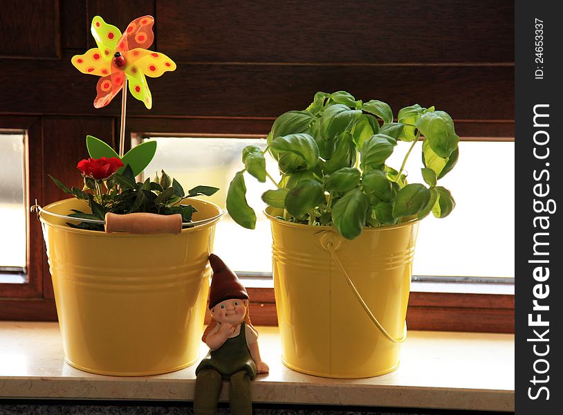 Two buckets containing a rose and basil on a windowsill with a dwarf sitting beside them. Two buckets containing a rose and basil on a windowsill with a dwarf sitting beside them