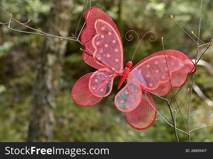 A red decoration butterfly on a branch in the forest. A red decoration butterfly on a branch in the forest.