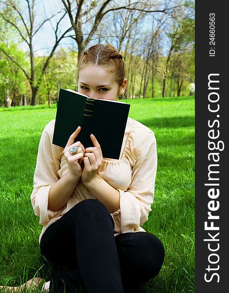 Woman hides her face behind a book sitting on green grass. Woman hides her face behind a book sitting on green grass