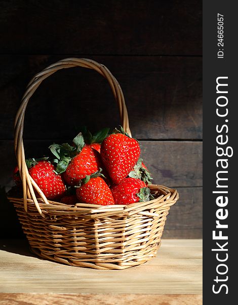 Wicker basket full of strawberries on wooden background under sunbeam. Wicker basket full of strawberries on wooden background under sunbeam