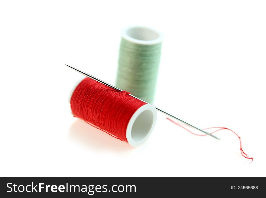 One red and green thread rolls with needle on white background. One red and green thread rolls with needle on white background