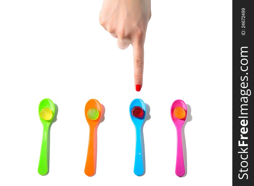 Female finger choosing between four colorful spoons with jellies. Female finger choosing between four colorful spoons with jellies.