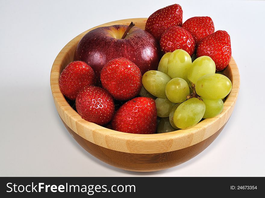 Apple with grapes and strawberries in wooden dish