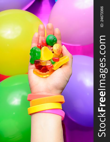 Woman's hand offering a lot of colorful candies over a group of ballons in a party concept image. Woman's hand offering a lot of colorful candies over a group of ballons in a party concept image.