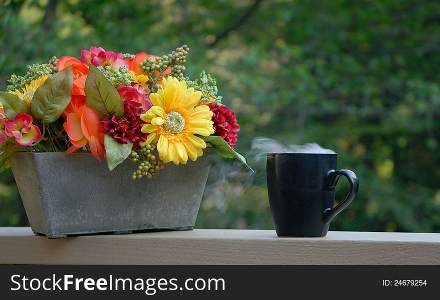 Steaming coffee on front porch next to flower basket. Steaming coffee on front porch next to flower basket
