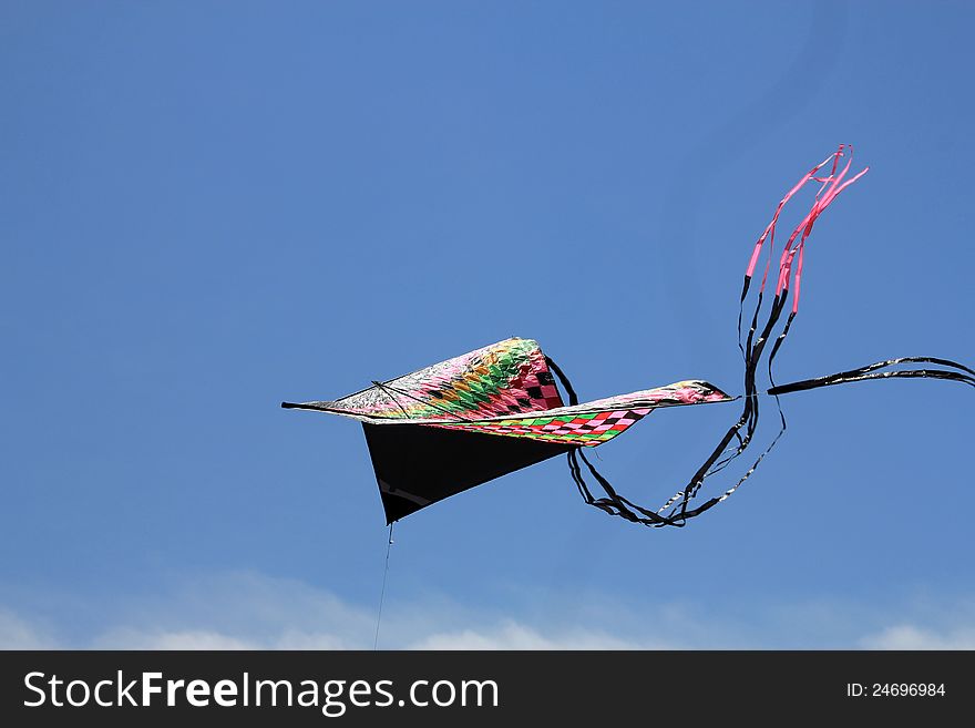 The colorful triangle kite with tail flying in blue sky. The colorful triangle kite with tail flying in blue sky