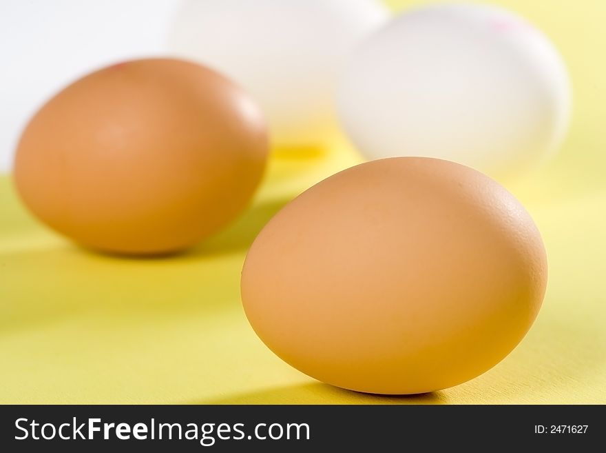 Some brown and white eggs on yellow background. Focus on the front egg. Some brown and white eggs on yellow background. Focus on the front egg.