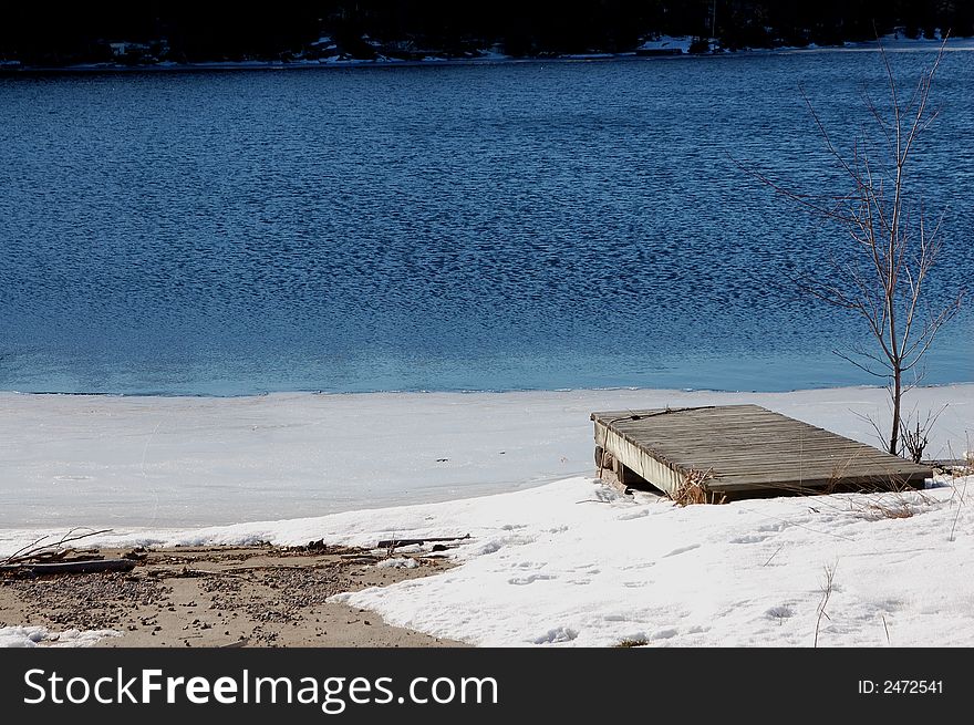 A gray dock juts diagonally into a pristine, half-frozen lake in Miners Bay. A gray dock juts diagonally into a pristine, half-frozen lake in Miners Bay