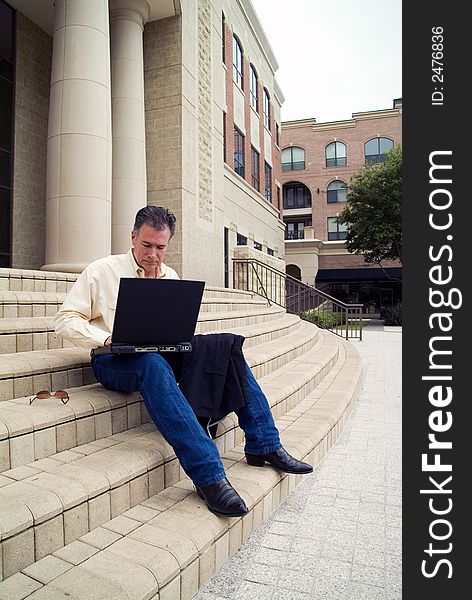 A man on the steps of a large building with working with a laptop. A man on the steps of a large building with working with a laptop.