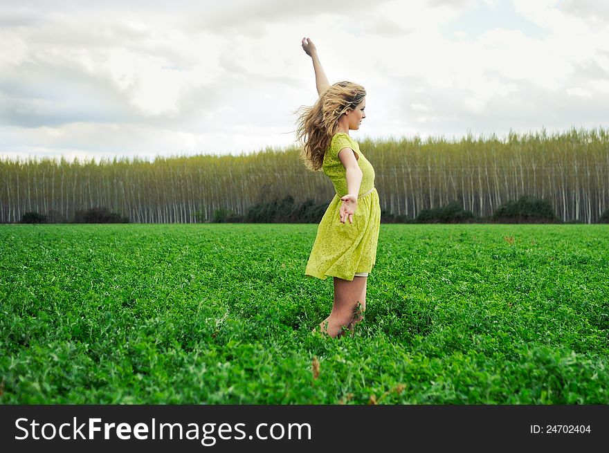 Portrait of a beautiful blonde girl, dressed with a green dress, with open arms in a meadow. Portrait of a beautiful blonde girl, dressed with a green dress, with open arms in a meadow