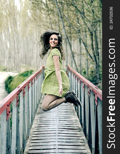 Beautiful blonde girl, dressed with a green dress, jumping in a rural bridge. Beautiful blonde girl, dressed with a green dress, jumping in a rural bridge