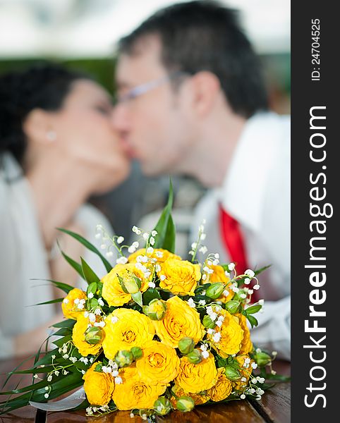 Newly-married couple and wedding bouquet in the foreground. Yellow roses bouquet