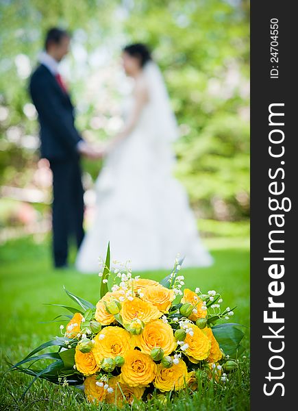 Newly-married couple and wedding bouquet in the foreground. Yellow roses bouquet