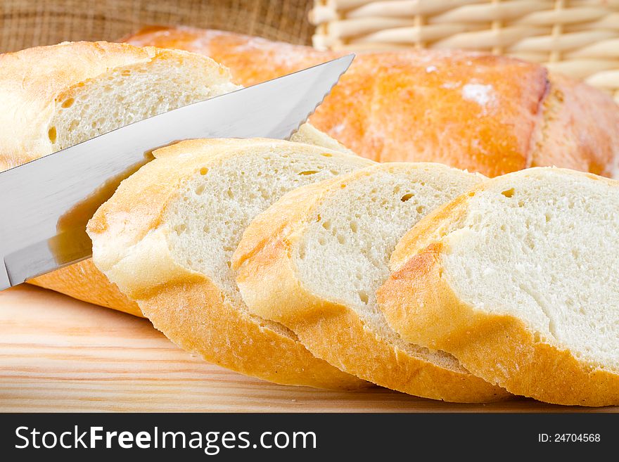 Freshly baked baguette sliced on wooden cutting board, knife. Freshly baked baguette sliced on wooden cutting board, knife