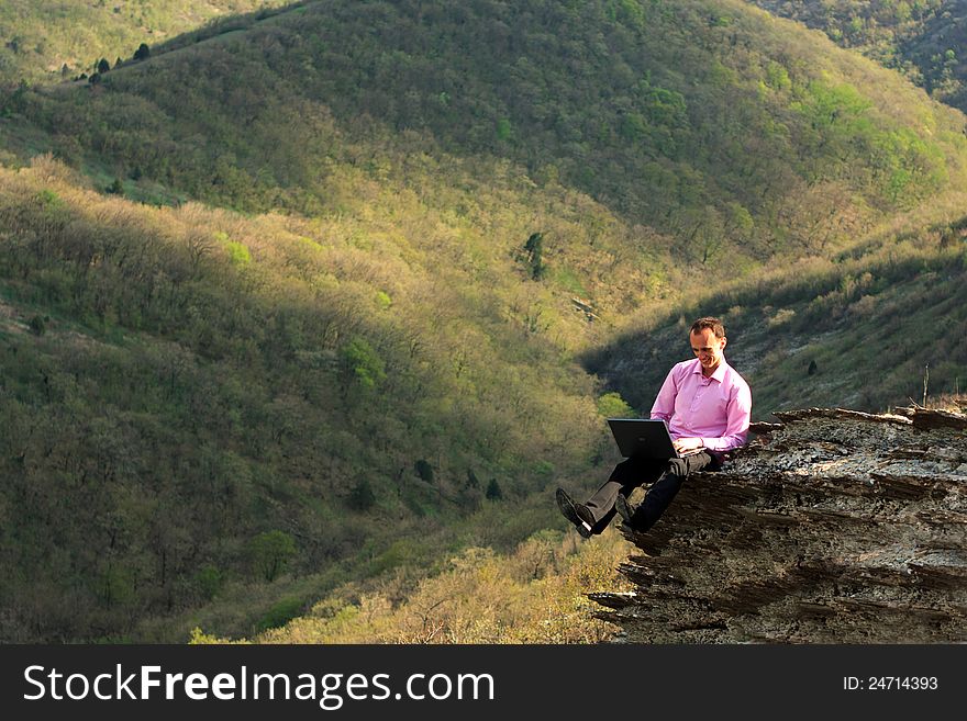 Man works for computer sitting on stone in mountains. Man works for computer sitting on stone in mountains