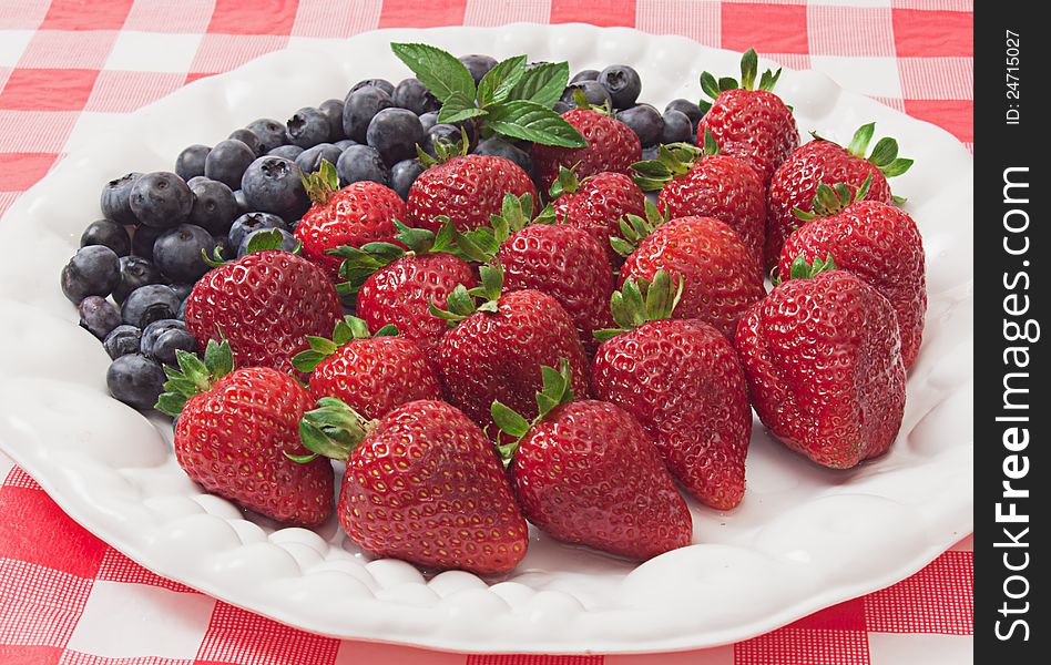 Luscious nutritious strawberries and blueberries arranged on white plate on checkered cloth. Luscious nutritious strawberries and blueberries arranged on white plate on checkered cloth.