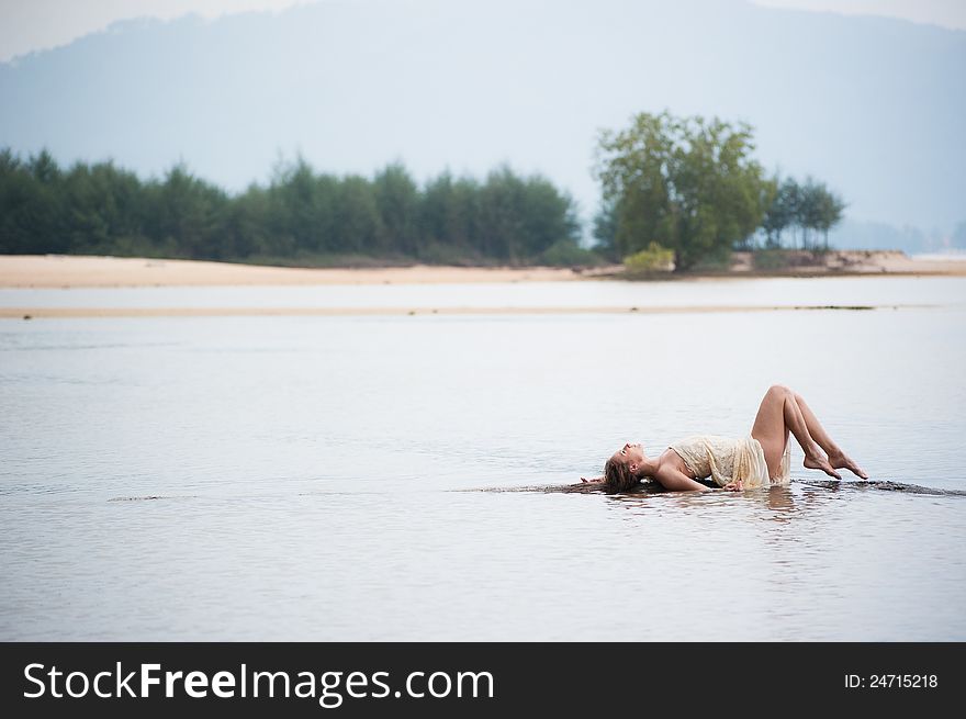 a beautiful young girl in white dress lying on a log in the water. a beautiful young girl in white dress lying on a log in the water