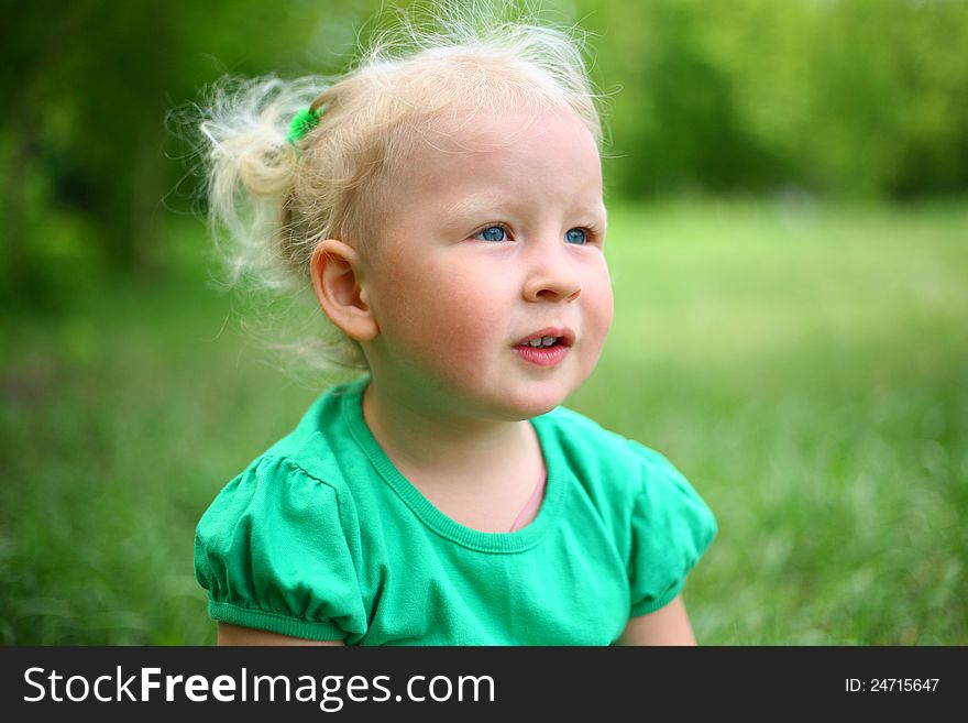 Child is sitting on the grass on a background of nature