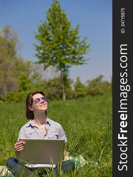 Young woman with laptop on a green grass in the park