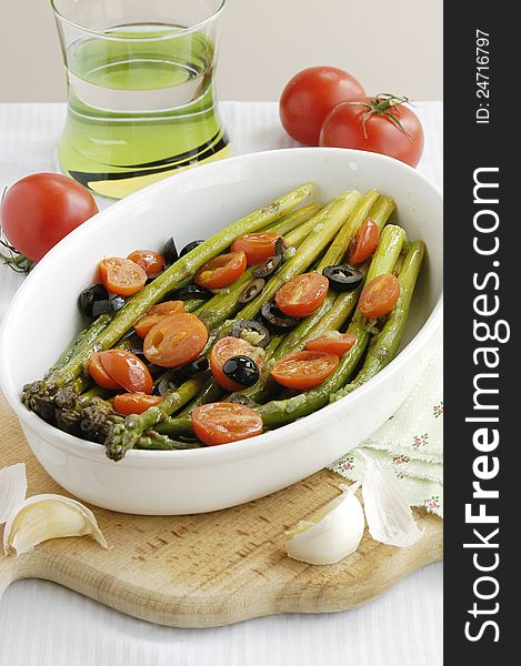 Asparagus baked with cherry tomatos, black olives and garlic served in plate. Asparagus baked with cherry tomatos, black olives and garlic served in plate