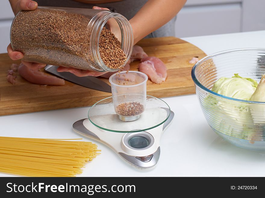 Female hands pouring buckwheat from pot in glass, that standing on scales