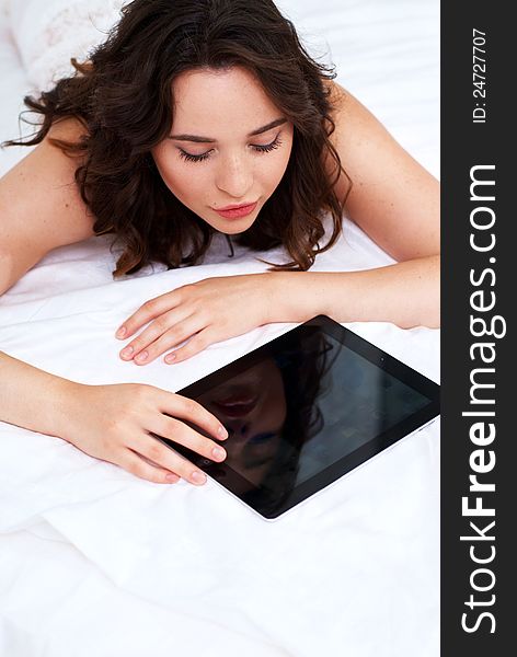 Beautiful emotional young woman using tablet computer in her bedroom high key. Beautiful emotional young woman using tablet computer in her bedroom high key